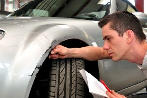 Carrossier qui inspecte une aile de voiture accidentée